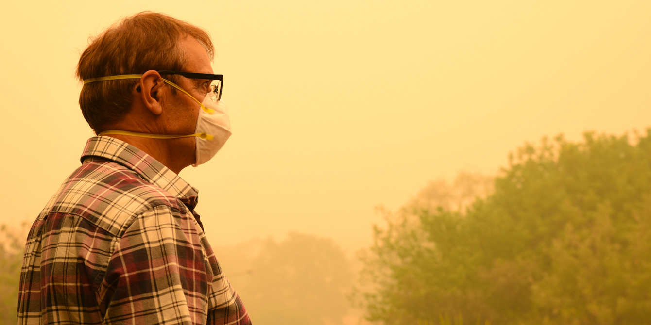 Man wearing N95 mask outside with a sky yellowed by smoke from nearby wildfires.